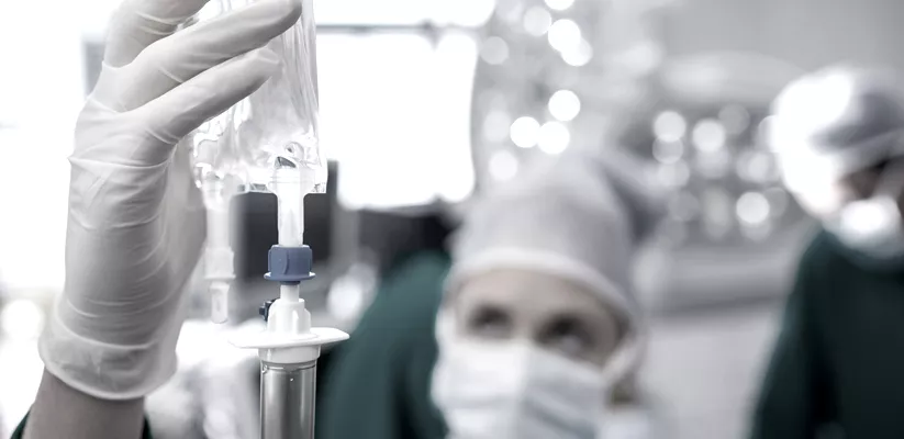 close-up of a person wearing a mask and gloves holding a iv drip